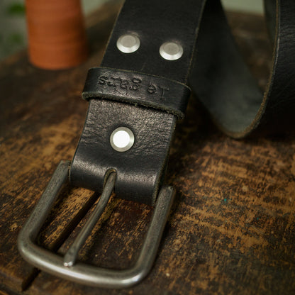 Black leather belt with metal buckle on a wooden surface