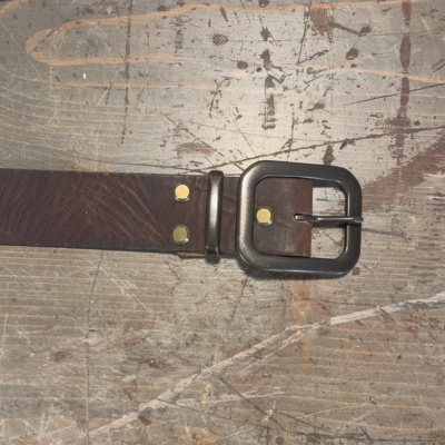Brown leather belt with a black buckle on a scratched wooden surface.