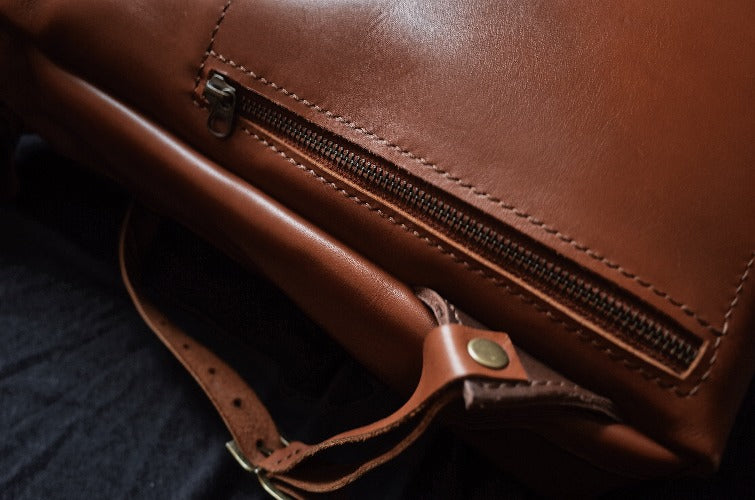 Sleek saddle tan leather roll-top backpack designed for travel and work

